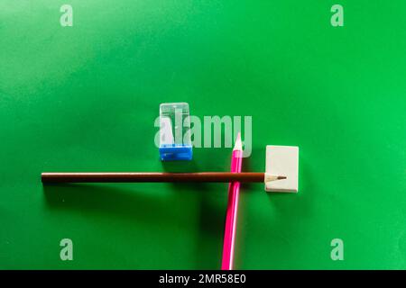 Una matita marrone e una rosa con una gomma e un affilatore. Isolato su sfondo verde. Foto Stock