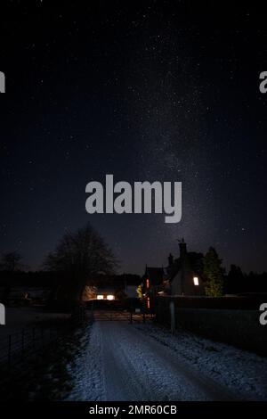 La Via Lattea che sorge su alcuni cottage in una scena invernale paesaggio notturno Foto Stock