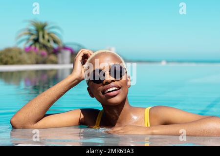 Ritratto di felice ragazza afro-americana che indossa occhiali da sole in piscina Foto Stock