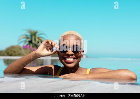 Ritratto di felice ragazza afro-americana che indossa occhiali da sole in piscina Foto Stock