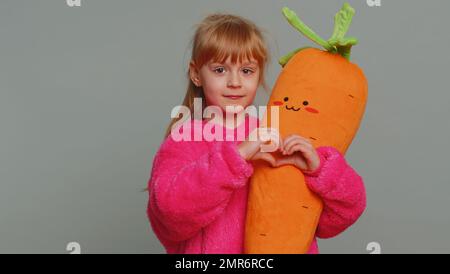 Ti voglio bene. Sorridente giovane preteen ragazza bambino capretto fa il gesto del cuore dimostra segno di amore esprime le buone sensibilità e la simpatia. Bambini piccoli che tengono il giocattolo isolato su sfondo grigio studio Foto Stock