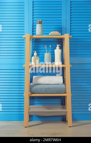 Scaffalatura in legno con articoli da bagno vicino a schermo pieghevole blu. Elemento interno del bagno Foto Stock