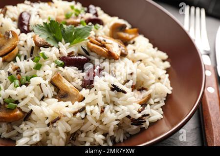 Delizioso pilaf di riso con funghi e fagioli in piatto, primo piano Foto Stock