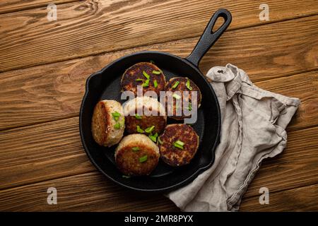 Cotolette fatte in casa di pesce, pollo o carne su una padella in ghisa nera padella padella padella su un tavolo di legno rustico, tradizionale pasto arrosto salubre cotolette in Foto Stock