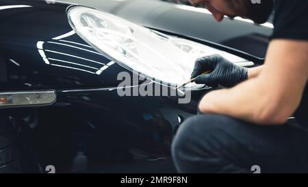 Delicati ritocchi di vernice per auto nera eseguiti con una piccola spazzola nell'area dei fari. Esperto di dettaglio delle auto durante il lavoro. Foto di alta qualità Foto Stock