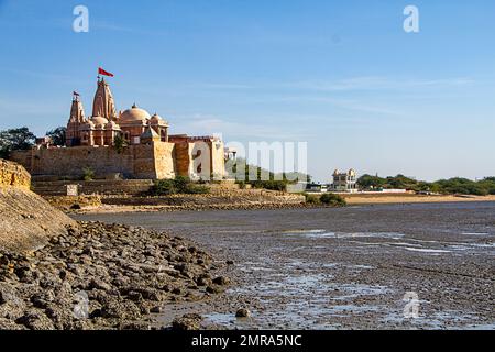 Tempio di Koteshwar con pendente rosso che vola in cima situato a Koteshwar Gujarat al torrente Kori durante la bassa marea Foto Stock