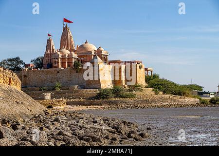 Tempio di Koteshwar con pendente rosso che vola in cima situato a Koteshwar Gujarat al torrente Kori durante la bassa marea Foto Stock