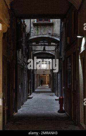 Un vicolo vuoto e scuro con una figura sola in lontananza nella città di Venezia. Foto Stock