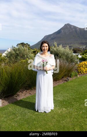 Ritratto verticale di felice sposa asiatica che tiene bouquet sorridente al matrimonio all'aperto, spazio copia Foto Stock