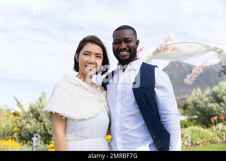 Ritratto di sposa felice e variegata sorridendo alla fotocamera durante il matrimonio all'aperto Foto Stock