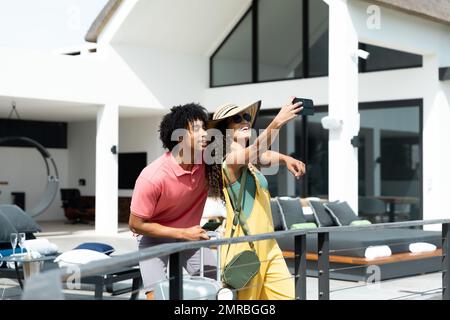 Felice coppia biraciale in arrivo fuori vacanza con valigia prendere selfie, spazio copia Foto Stock