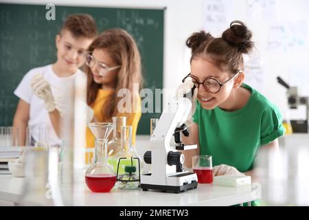 Studentessa che guarda attraverso il microscopio e i suoi compagni di classe alla classe chimica Foto Stock