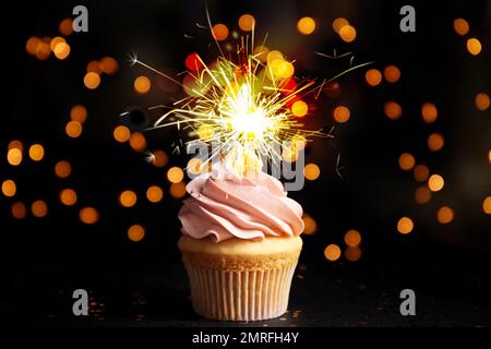 Delizioso cupcake di compleanno con brillantezza sul tavolo nero contro le luci sfocate Foto Stock