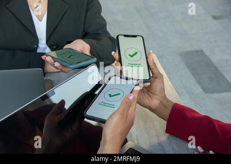 Primo piano delle mani di tre donne che pagano il conto con i loro smartphone. Pagamento completato Foto Stock
