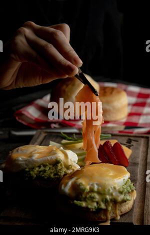 Un colpo verticale di una persona che aggiunge salmone sulle uova di benedict Foto Stock