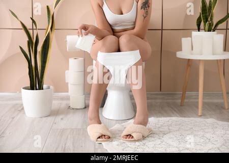 Giovane donna con imbottitura mestruale seduta sul water in bagno Foto Stock