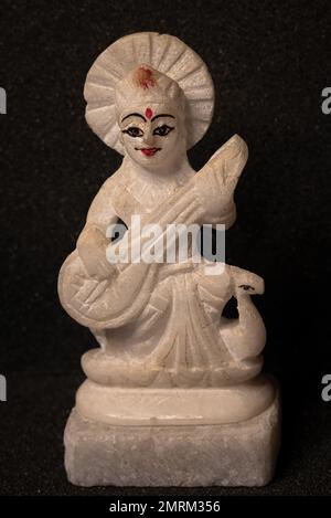 Primo piano immagine della dea Saraswati idolo fatto da pietra bianca isolato su sfondo nero, devi Saraswati considerato come la dea della conoscenza, mus Foto Stock