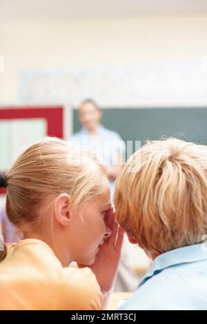 È un segreto...la vista posteriore di due studenti che condividono un segreto in classe. Foto Stock