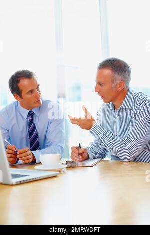 Dirigenti che discutono la proposta sul caffè. Uomini d'affari che discutono con il notebook davanti a loro. Foto Stock