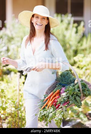 Fiero del suo raccolto fresco. Una donna splendida tiene un cestino di verdure appena raccolte nel suo giardino. Foto Stock