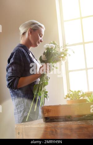 I fiori illuminano il mondo. una giovane donna che tiene un mazzo di fiori mentre si trova accanto a una finestra all'interno. Foto Stock