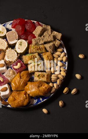 Un grande piatto di vari dolci orientali e noci su uno sfondo scuro Foto Stock