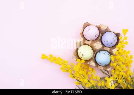 Uova multicolore dipinte con ramo di mimosa su sfondo rosa. Vista dall'alto. Pasqua. Spazio di copia Foto Stock