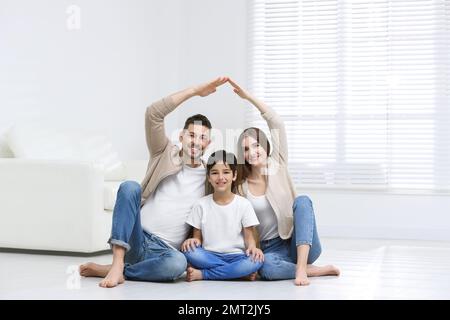 Famiglia felice che forma il tetto della casa con le loro mani a casa. Concetto di assicurazione Foto Stock