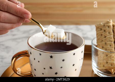 Donna aggiungendo raffinati cubetti di zucchero al tè aromatico a tavola, primo piano Foto Stock