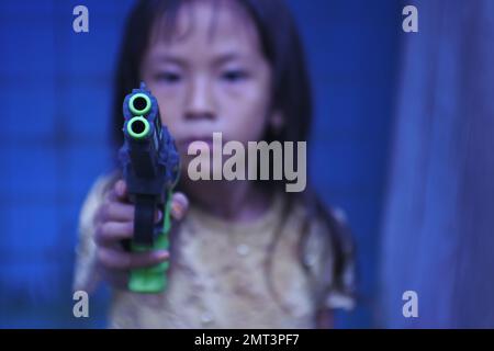 Una ragazza triste che punta una pistola giocattolo sulla fotocamera in una messa a fuoco selettiva Foto Stock