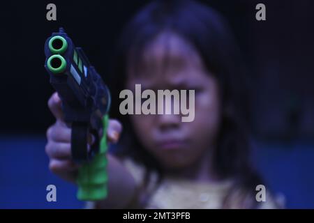 Una ragazza triste che punta una pistola giocattolo sulla fotocamera in una messa a fuoco selettiva Foto Stock