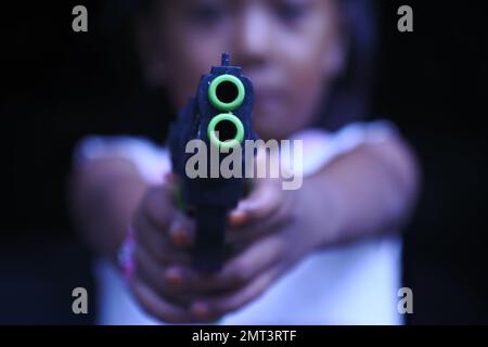 Una ragazza triste che punta una pistola giocattolo sulla fotocamera in una messa a fuoco selettiva Foto Stock