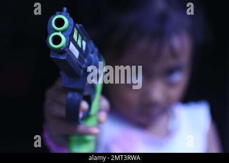 Una ragazza triste che punta una pistola giocattolo sulla fotocamera in una messa a fuoco selettiva Foto Stock