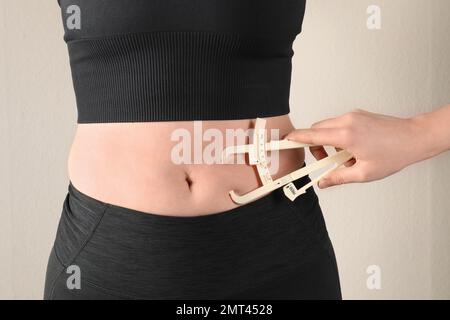 Nutrizionista misurazione dello strato di grasso corporeo della donna con calibro su sfondo beige, primo piano Foto Stock
