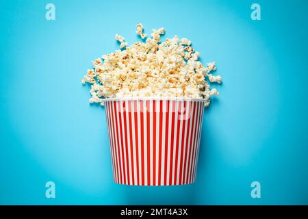 Secchio di carta rovesciato con delizioso popcorn su sfondo azzurro, vista dall'alto Foto Stock