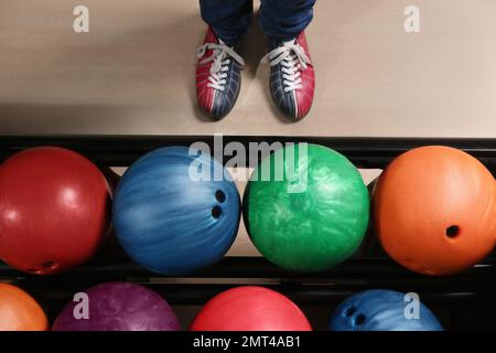 Persona in scarpe da bowling vicino al rack con palle, vista dall'alto Foto Stock