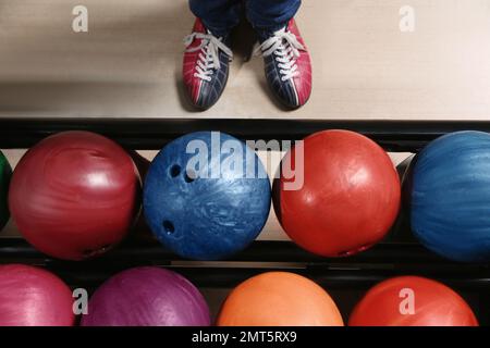 Persona in scarpe da bowling vicino al rack con palle, vista dall'alto Foto Stock