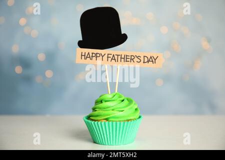 Cupcake con cappello di carta e targhetta HAPPY FATHER's DAY su tavolo bianco su sfondo sfocato Foto Stock