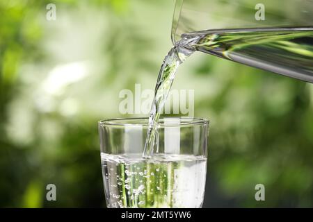 Versare l'acqua dalla caraffa nel vetro su sfondo sfocato Foto Stock