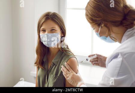 Bambino adolescente felice in maschera medica che viene vaccinato contro l'infezione virale Foto Stock