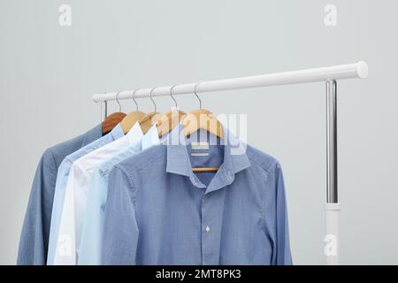 Rack con eleganti abiti da uomo su sfondo chiaro Foto Stock