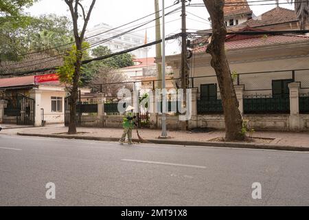 Hanoi, Vietnam, gennaio 2023. una spazzatrice stradale con un tradizionale cappello di paglia pulisce la strada in una strada nel centro della città Foto Stock