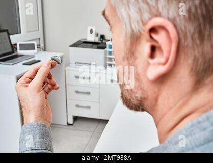 Paziente di sesso maschile con problemi di udito che tiene gli apparecchi acustici mentre si trova nell'ufficio del medico presso la clinica uditiva. Apparecchi acustici Foto Stock