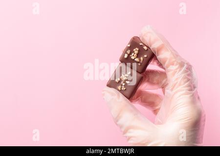 Bonbonbon di cioccolato dipinti a mano in una mano umana. Delizioso dessert su sfondo rosa con copyspace Foto Stock