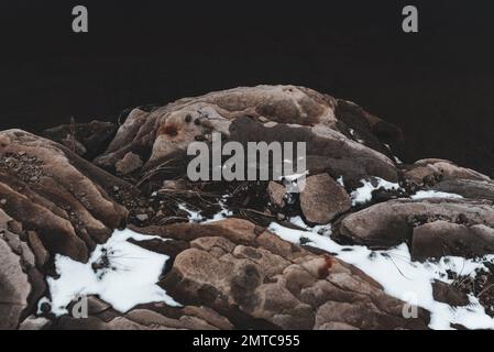 Affioramento di roccia sulla riva con neve e tracce di ruggine dalle pietre. Foto Stock