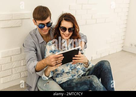 Felice coppia con il tablet, shopping online, fare l'ordine Internet seduto a casa piano in soggiorno vuoto Foto Stock