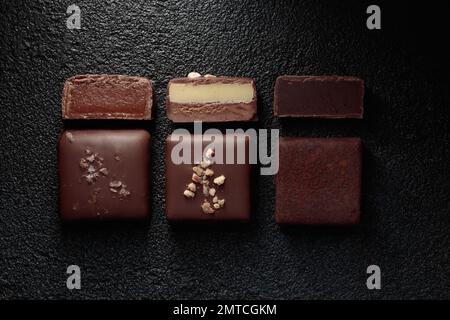 Fila di bonbon al cioccolato fatti a mano e pezzi di caramelle tagliate con pralina e tartufo su sfondo nero con banner orizzontale copyspace Foto Stock