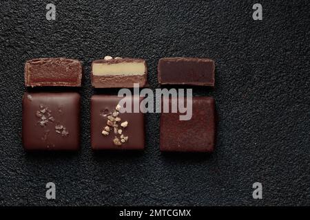 Fila di bonbon al cioccolato fatti a mano e pezzi di caramelle tagliate con pralina e tartufo su sfondo nero con banner orizzontale copyspace Foto Stock