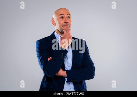 Pensando a un uomo di mezza età che indossa cravatta e blazer mentre si trova su uno sfondo bianco isolato. Spazio di copia. Foto Stock