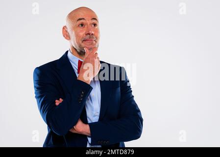 Pensando a un uomo di mezza età che indossa cravatta e blazer mentre si trova su uno sfondo bianco isolato. Spazio di copia. Foto Stock